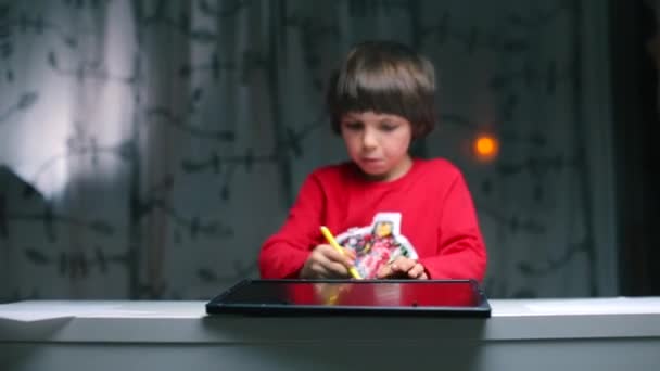 Um menino sentado em uma mesa desenha um teclado e um tablet com um lápis . — Vídeo de Stock