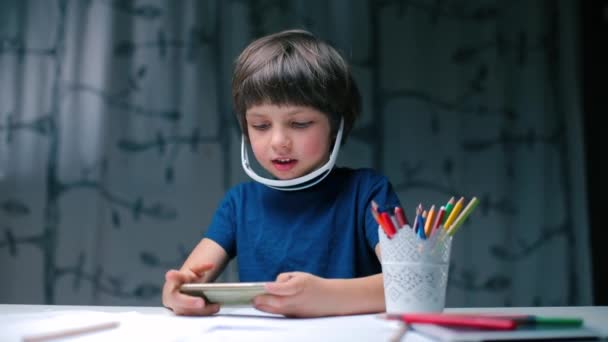 The boy plays an electronic game while sitting at the table. — 비디오