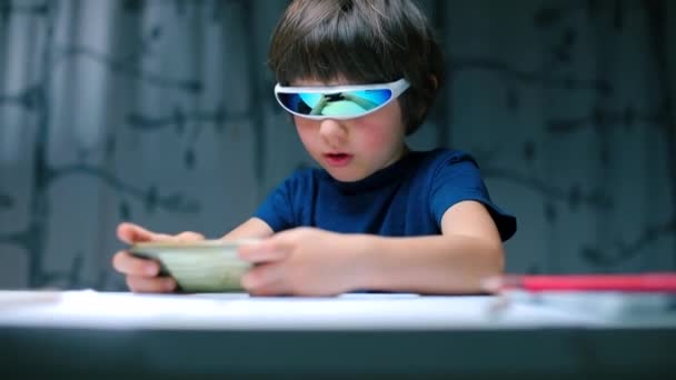 A boy sitting at a table with glasses uses a smartphone — 비디오