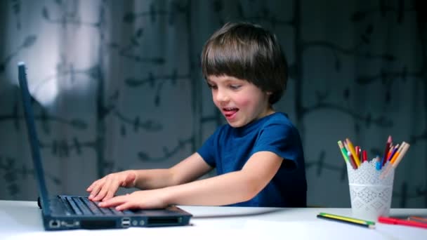 O menino sentado na mesa pressiona aleatoriamente as teclas do teclado . — Vídeo de Stock
