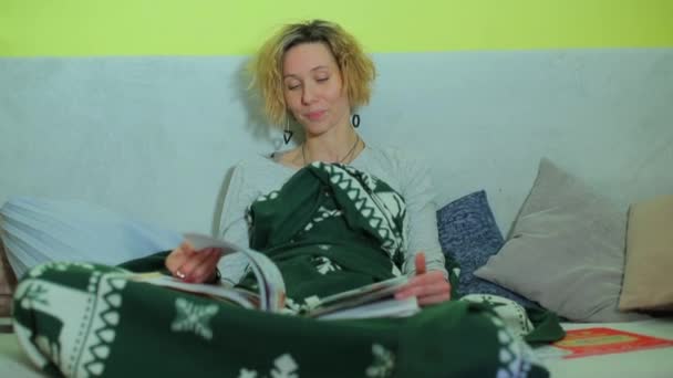 Весела жінка сидить на дивані, залишаючи через книгу . — стокове відео