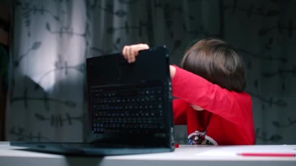 Un garçon répare un ordinateur portable assis à une table . — Video