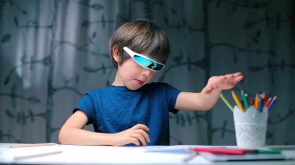 Um menino de óculos modernos sentado em uma mesa mostra um gesto como . — Vídeo de Stock