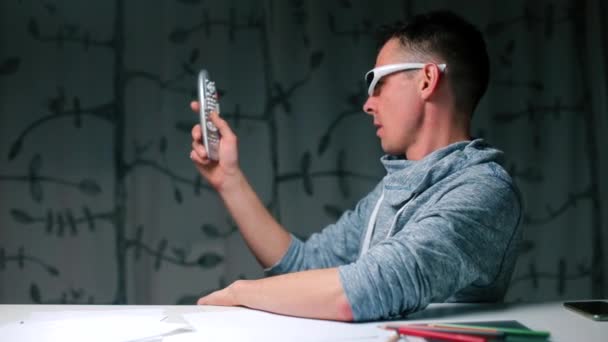 Um homem de óculos modernos assume um controle remoto em sua mão — Vídeo de Stock