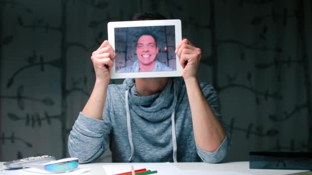 Un tipo sentado en una mesa sostiene la pantalla de la tableta en sus manos en lugar de su cabeza . — Vídeo de stock