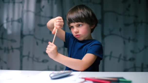 Un enfant joue avec un crayon assis à une table à l'école . — Video