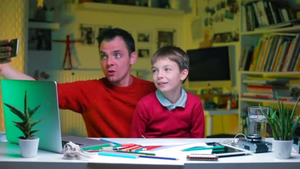 Video blogger hace un blog con un niño de rodillas sentado a la mesa . — Vídeos de Stock