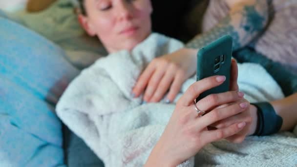 A woman writes a text message on a smartphone while lying in a sofa. — Stock Video