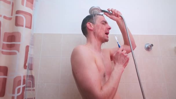 Der Typ wäscht sich unter der Dusche und singt ein Lied auf der Zahnbürste. — Stockvideo