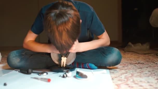 En pojke som sitter på golvet reparerar elektrisk utrustning. — Stockvideo