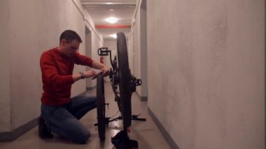 Bir adam bisiklet tekerleğini söker ve kameraya bakar..