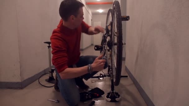 Um homem gira uma roda de bicicleta em uma garagem . — Vídeo de Stock