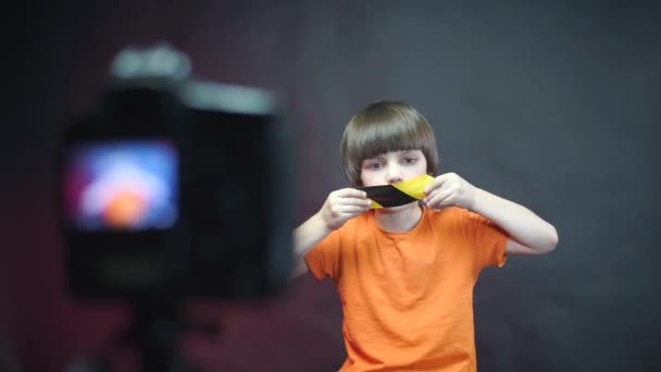 El niño sella su boca con cinta adhesiva delante de la videocámara . — Vídeo de stock