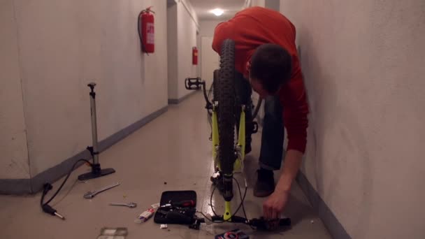 A man makes repairs to a bicycle in the basement of an apartment building. — Stock Video