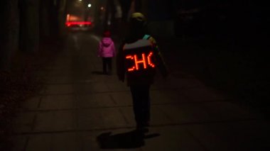 Parlak sırt çantalı öğrenci kız kardeşiyle birlikte yolda yürüyor..