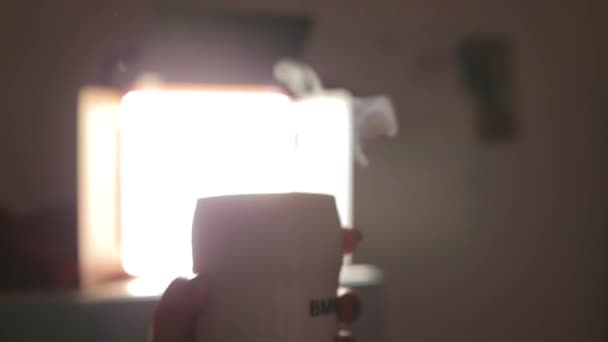 Närbild av en mugg med varmt kaffe mot bakgrund av bakgrundsbelysning. — Stockvideo