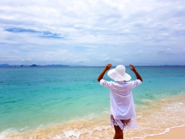 Girl on the seashore in a white dress and hat. Back view.