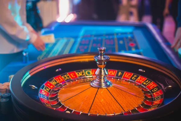 Una imagen vibrante de cerca de la mesa de casino multicolor con la ruleta en movimiento, con la mano de crupier, y un grupo de personas ricas en juegos de azar —  Fotos de Stock