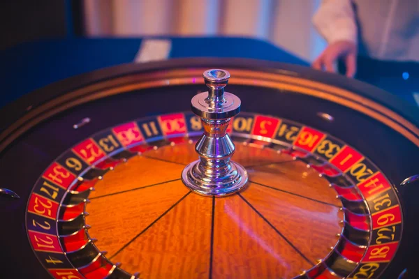 Una imagen vibrante de cerca de la mesa de casino multicolor con la ruleta en movimiento, con la mano de crupier, y un grupo de personas ricas en juegos de azar —  Fotos de Stock