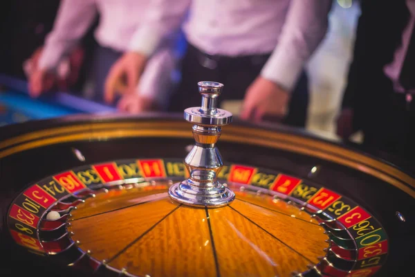 Ein lebendiges Bild aus nächster Nähe von einem bunten Casino-Tisch mit Roulette in Bewegung, mit der Hand eines Croupier und einer Gruppe reicher Glücksspieler — Stockfoto