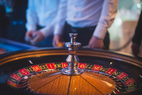 Ein lebendiges Bild aus nächster Nähe von einem bunten Casino-Tisch mit Roulette in Bewegung, mit der Hand eines Croupier und einer Gruppe reicher Glücksspieler — Stockfoto