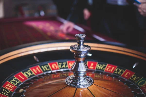 Ein lebendiges Bild aus nächster Nähe von einem bunten Casino-Tisch mit Roulette in Bewegung, mit der Hand eines Croupier und einer Gruppe reicher Glücksspieler — Stockfoto