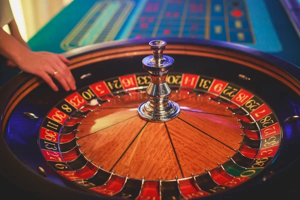 Una imagen vibrante de cerca de la mesa de casino multicolor con la ruleta en movimiento, con la mano de crupier, y un grupo de personas ricas en juegos de azar —  Fotos de Stock