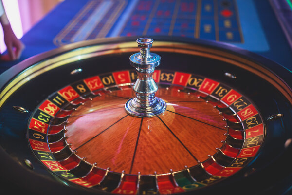 A close-up vibrant image of multicolored casino table with roulette in motion, with the hand of croupier, and a group of gambling rich wealthy people 