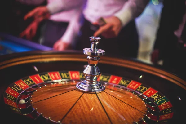 Ein lebendiges Bild aus nächster Nähe von einem bunten Casino-Tisch mit Roulette in Bewegung, mit der Hand eines Croupier und einer Gruppe reicher Glücksspieler — Stockfoto