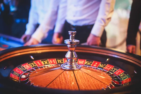 Ein lebendiges Bild aus nächster Nähe von einem bunten Casino-Tisch mit Roulette in Bewegung, mit der Hand eines Croupier und einer Gruppe reicher Glücksspieler — Stockfoto