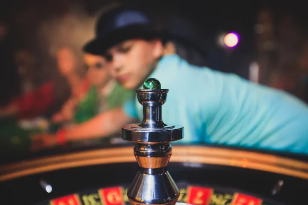 Una imagen vibrante de cerca de la mesa de casino multicolor con la ruleta en movimiento, con la mano de crupier, y un grupo de personas ricas en juegos de azar —  Fotos de Stock