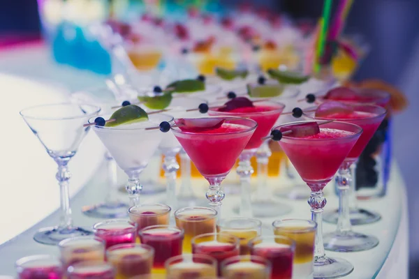 Όμορφη γραμμή γραμμή διαφορετικά χρωματισμένα αλκοόλ κοκτέιλ με δυόσμο σε ένα υπαίθριο πάρτι, μαρτίνι, βότκα με φυσαλίδες και άλλοι διακοσμημένα catering ανθοδέσμη γάμου τραπέζι σε υπαίθριο γεγονός, σε σχεδόν — Φωτογραφία Αρχείου