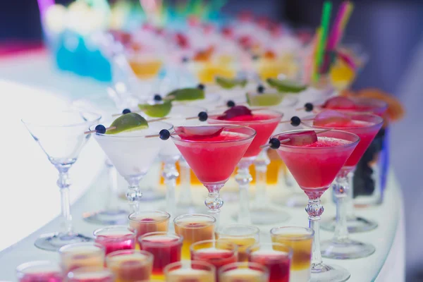 Beautiful row line of different colored alcohol cocktails with mint on a open air party, martini, vodka with bubbles,and others on decorated catering bouquet wedding table on open air event — Stock Photo, Image