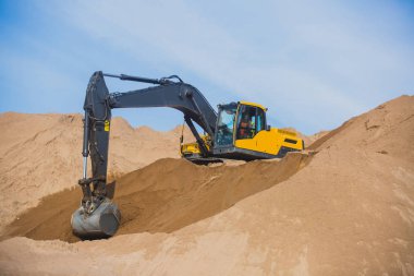 Yellow heavy excavator and bulldozer excavating sand and working during road works, unloading sand and road metal during construction of the new road clipart
