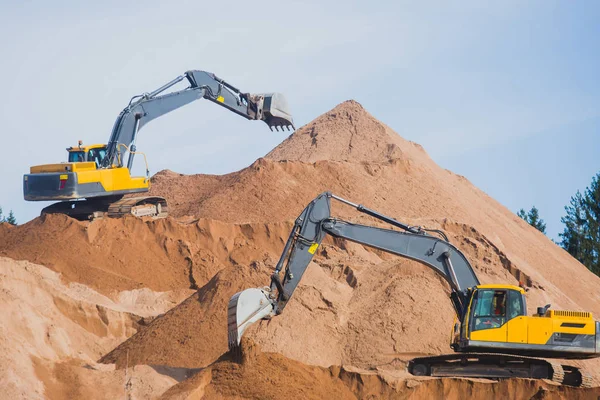 Escavadora pesada amarela e escavadora escavando areia e trabalhando durante obras rodoviárias, descarregando areia e metal rodoviário durante a construção da nova estrada — Fotografia de Stock