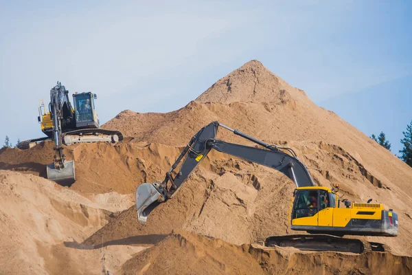 Escavadora pesada amarela e escavadora escavando areia e trabalhando durante obras rodoviárias, descarregando areia e metal rodoviário durante a construção da nova estrada — Fotografia de Stock