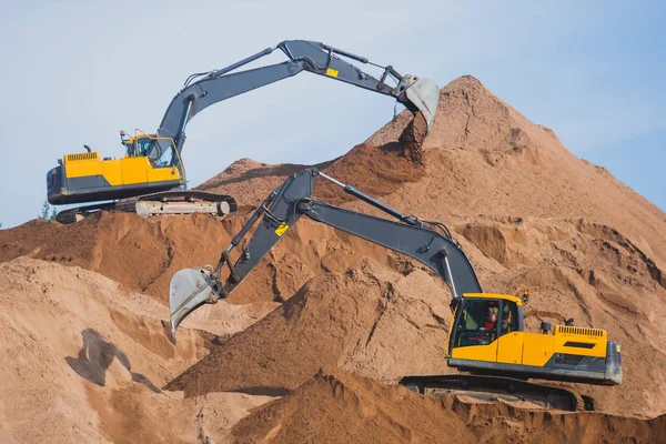 Escavadora pesada amarela e escavadora escavando areia e trabalhando durante obras rodoviárias, descarregando areia e metal rodoviário durante a construção da nova estrada — Fotografia de Stock