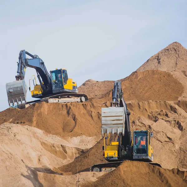 Жовтий важкий екскаватор і бульдозер розкопують пісок і працюють під час дорожніх робіт, розвантажуючи пісок і дорожній метал під час будівництва нової дороги — стокове фото