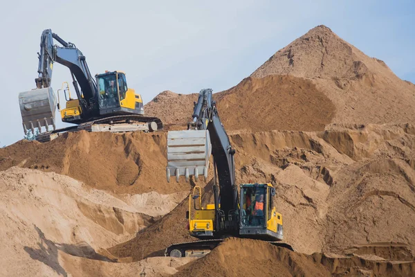 Escavadora pesada amarela e escavadora escavando areia e trabalhando durante obras rodoviárias, descarregando areia e metal rodoviário durante a construção da nova estrada — Fotografia de Stock