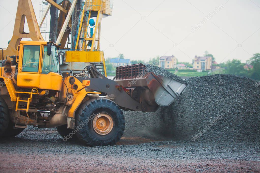 Yellow heavy excavator and bulldozer excavating sand and working during road works, unloading sand and road metal during construction of the new road