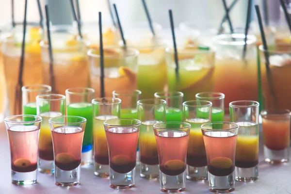 Linha de linha bonita de diferentes coquetéis de álcool coloridos em uma festa, martini, vodka e outros na mesa de buquê de catering decorada em evento ao ar livre, imagem com belo bokeh — Fotografia de Stock