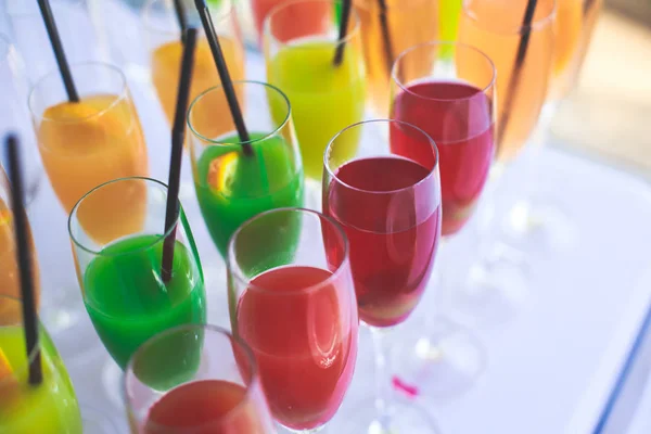 Beautiful row line of different colored alcohol cocktails on a party, martini, vodka,and others on decorated catering bouquet table on open air event, picture with beautiful bokeh — Stock Photo, Image