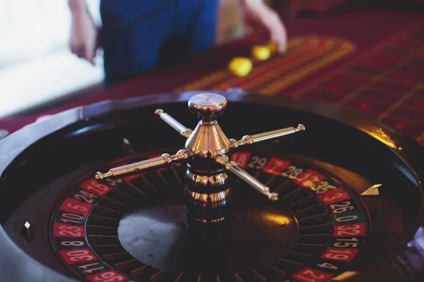 Eine Nahaufnahme lebendiges Bild von bunten Casino-Tisch mit Roulette in Bewegung, mit der Hand des Croupier, und eine Gruppe von Glücksspiel reichen reichen Menschen im Hintergrund — Stockfoto