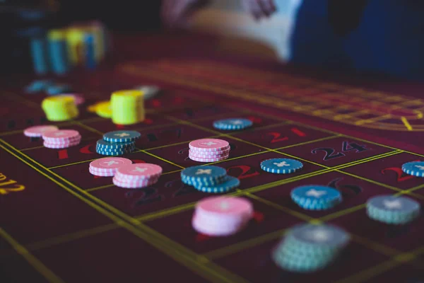 Крупный план яркого изображения разноцветного стола казино с рулеткой в движении, с рукой крупье, и группа азартных игр богатых богатых людей на заднем плане — стоковое фото