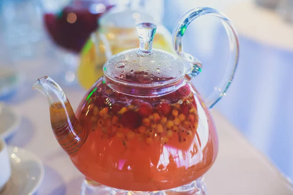 Mooie warme foto van transparante theepot waterkoker met smakelijke groen zwarte thee met appel, citroen en gember op een tabel met kaarsen en dessert op de achtergrond — Stockfoto