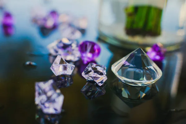 Diamond (small purple jewel) stones heap over mirror glass table, crystal stones, shiny gold and silver jewelery on a table