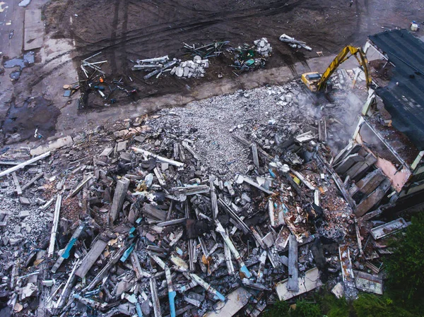 A process of buliding demolition, demolition site with heavy bulldozer and excavator with crushing equipment at work, demolished house, shot from air with drone