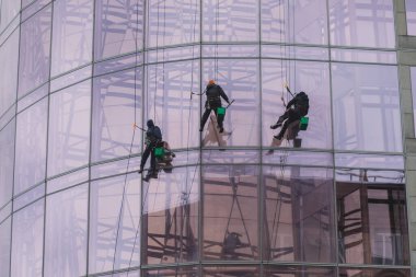 Yüksek binadaki pencereleri temizleyen bir grup işçi, endüstriyel dağcılar modern bir ofis binasının cam cephesini yıkıyorlar.