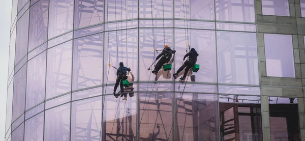 高層ビルの窓を掃除する労働者のグループ 近代的なオフィスビルのガラスのファサードを洗う産業の登山者 — ストック写真