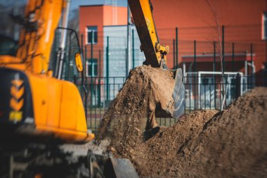 Sarı ağır kazıcı kumu kazıyor ve yol çalışmaları sırasında çalışıyor, yeni yolun inşaatı sırasında kumu boşaltıyor ve etrafta işçiler var.